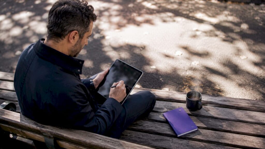 Installé dans un café, un entrepreneur peaufine son budget marketing, tablette et carnet à la main.